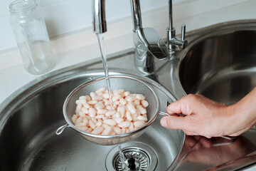 man rinses cooked white beans under tap water