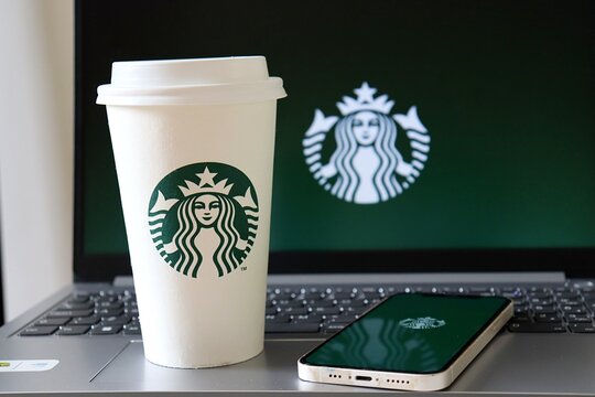 Starbucks Coffee Cup and smartphone in front of laptop with Starbucks Logo. 