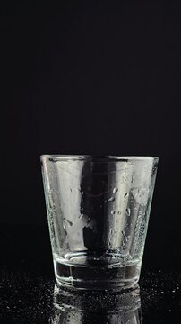 Hand in thin food-prep glove places wet empty glass on a black surface. Close-up view of hand wearing thin preparation glove placing glass. cleanliness, kitchen workflow and drink-making preparation.