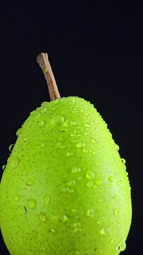 Green pear with water drops on black background vertical video. Symbolic fruit scene to vitamins, vegetarian nutrition, cooking ingredients, juice bar, recipe preparation.