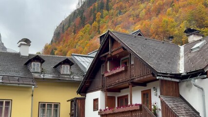 Picturesque view of traditional Alpine house rooftops and wooden architecture in Hallstatt, Austria, backed by a steep mountain slope covered in vibrant autumn colors.