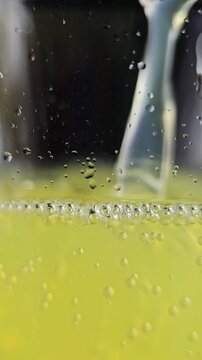 Yellow sparkling lemonade pouring into a glass in vertical close-up video. carbonated drink being poured into a glass, with visible bubbles, foam and fizzing liquid in a detailed macro shot