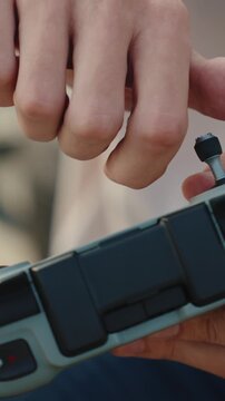 A man screws a joystick into a drone controller in a vertical close-up shot on a sunny outdoor day.