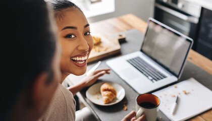 Joyful woman enjoying morning coffee and croissant while working on laptop at home, radiating happiness and productivity in a modern lifestyle scene