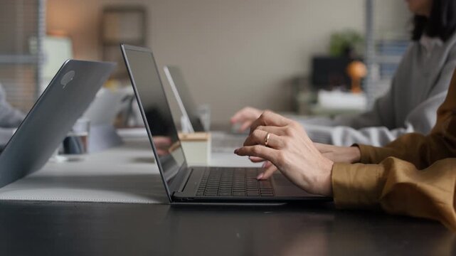 Cropped shot of hands of unrecognizable female employees typing on laptops sitting at one desk in office workplace