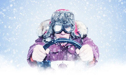 Man in a winter coat and fur hat gripping a steering wheel in a heavy snowstorm, wearing icy goggles and facing extreme cold, symbolizing harsh winter driving conditions.