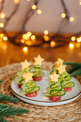 Delicious Christmas appetizer shaped like Christmas trees with cheese, cucumber, salami and festive background