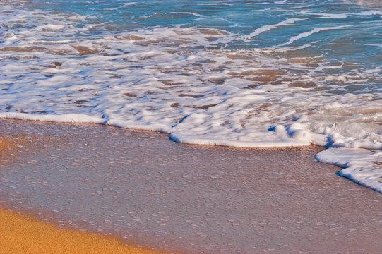 Foaming ocean waves washing golden beach sand