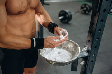 Preparing for competition. Fitness man is rubbing his hands with chalk, specifically magnesium...