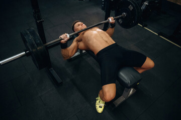 Lying down and pushing the barbell. Athletic man performing weightlifting exercises in a gym