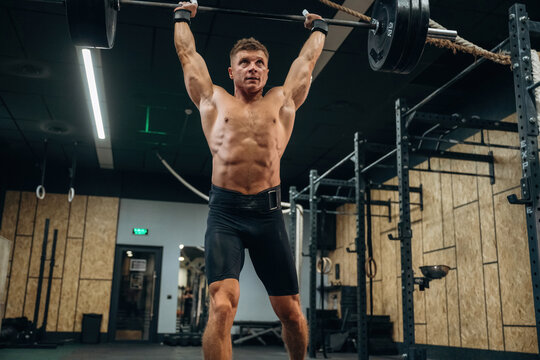 Made it, heavy barbell is high up in the hands. Athletic man performing weightlifting exercises