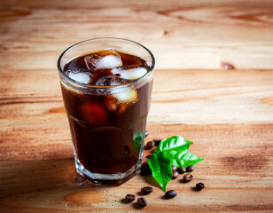 A glass of black iced coffee with ice cubes on a wooden surface. Ai