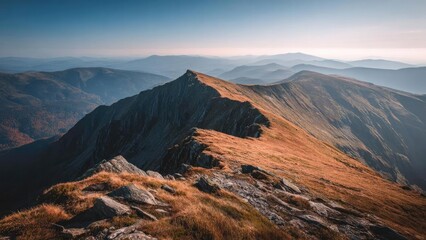 Naklejka premium Rocky mountain ridge bathed in autumn light, a narrow path winds along golden grasses toward distant blue-hazed peaks. Concept Autumn Mountain Ridge, Golden-Grass Trail, Narrow Mountain Path