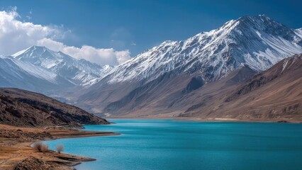 Snow-capped mountains rise over a vivid turquoise lake with brown, barren shores. Concept Snow-capped mountains, Turquoise alpine lake, Brown barren shores, Mountain reflection, Dramatic landscape