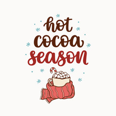 Hot cocoa season hand lettering and a cup of cocoa with marshmallows, wrapped in a scarf. Hygge and winter vibes concept