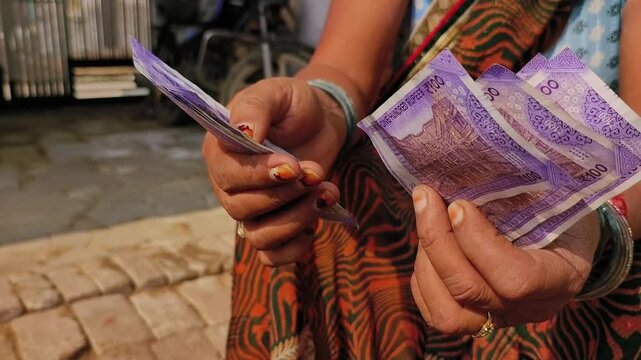 An indian woman counting 100 rupees indian currency notes.