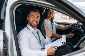 Gesture of thumb up, smiling. Woman is with instructor in car, driving school concept