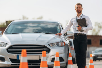 Leaning on the car. Driving school worker is outdoors