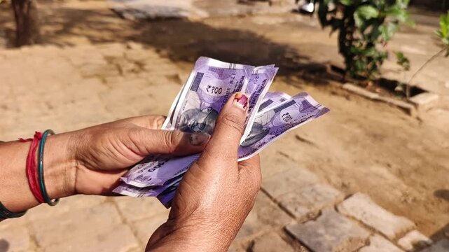 An indian woman counting 100 rupees indian currency notes.