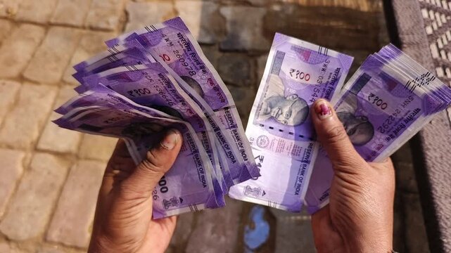 An indian woman counting 100 rupees indian currency notes.