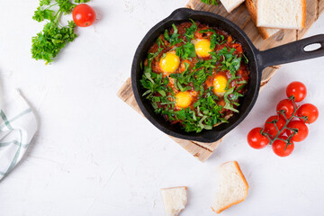 Shakshouka with quail eggs and tomato sauce topped with herbs served in cast iron pan on a white table. Middle Eastern and African meal. Top view. Copy space