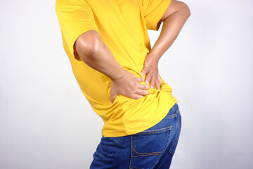 Lower back pain, close-up of a young man experiencing lower back pain after working at home. An adult man holding his lower back, chronic back pain, bone calcification, osteoporosis.Healthcare concept