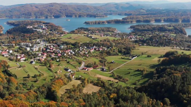 Aerial drone view of Polańczyk village and Solina Lake in Bieszczady Mountains, Poland. Scenic autumn landscape featuring rolling hills and forested shoreline.