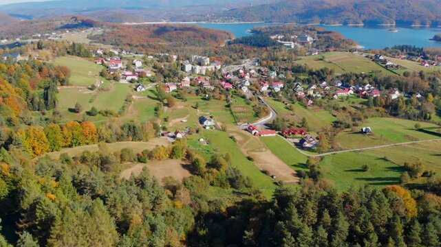 Aerial drone view of Polańczyk village and Solina Lake in Bieszczady Mountains, Poland. Scenic autumn landscape featuring rolling hills and forested shoreline.