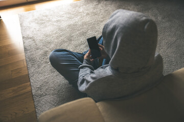 A Young Person Engaged with Their Smartphone While Sitting on the Floor in a Cozy and Isolated Indoor Setting