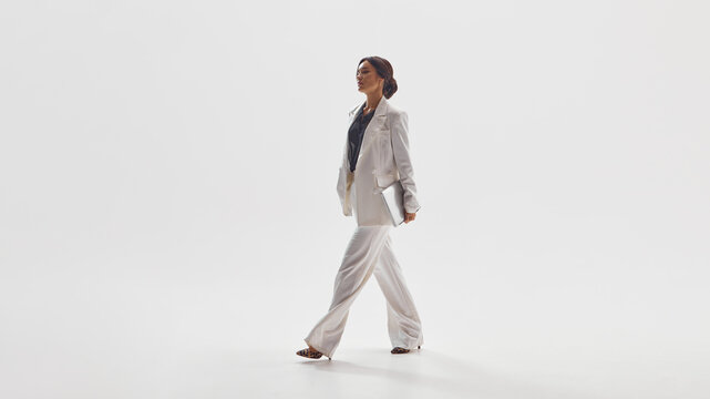 Stylish woman in white suit walking confidently representing success and power in modern fashion. Concept of luxury business aesthetics, empowerment, elegance for editorial and lifestyle use.