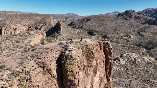 Aerial view of a stunning desert landscape featuring a towering cliffside with people standing on top, bathed in the golden light, Apache Junction, Arizona, United States.