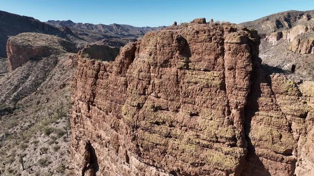 Aerial view of rugged, rocky cliffs, displaying a contrast of red and green hues, against a backdrop of arid desert landscape, Apache Junction, Arizona, United States.