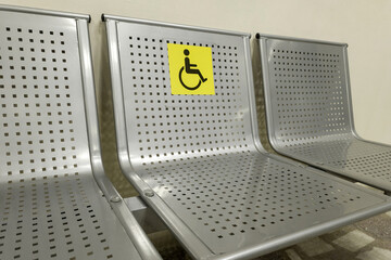Disabled seats at the train station. Metal seats with a special yellow sign depicting a person in a wheelchair