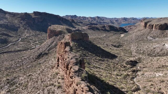 Aerial view of rugged cliffs, desert vegetation, and a distant lake under a clear blue sky, Apache Junction, Arizona, United States.