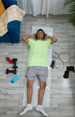 Top view of a young man lying on the exercise mat with his eyes closed, listening to music and resting after exercising. A moment of relaxation and well being