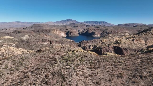 Aerial view of Canyon Lake surrounded by rugged desert mountains under a clear blue sky, showing contrasting textures and tones, Apache Junction, Arizona, United States.