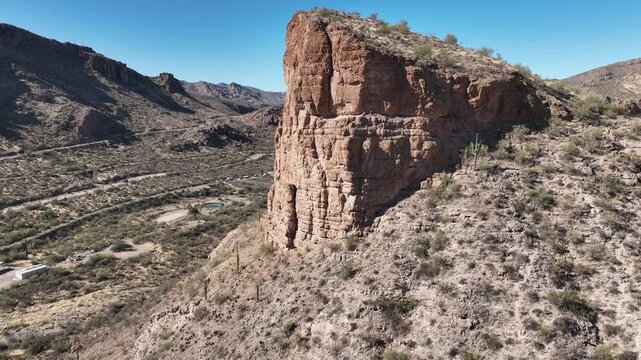 Aerial view of a rugged cliffside landscape featuring a towering rock formation with desert vegetation, juxtaposed against a clear blue sky, Apache Junction, Arizona, United States.