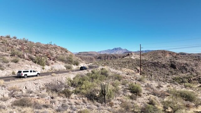 Aerial view of a lone white truck winding through the apache trail cutting through the arid landscape, under a bright blue sky, Apache Junction, Arizona, United States.