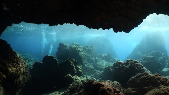  scuba divers exploring around a reef underwater deep blue water big rocks and bubbles ocean scenery 