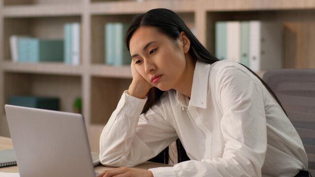 Pensive sad upset dreaming Asian Japanese business woman female girl Korean businesswoman manager hr office worker working laptop computer desk think imagine dream bored boring work melancholy indoor - Powered by Adobe