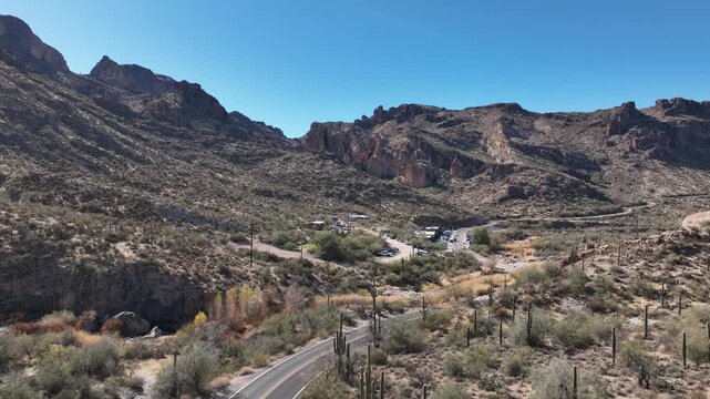 Aerial view of a winding road cuts through the arid landscape, nestled between rugged mountains under a clear, azure sky, Apache Junction, Arizona, United States.