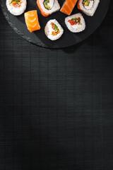 Philadelphia sushi roll salmon on round slate board and black bamboo mat in soft sunlight.