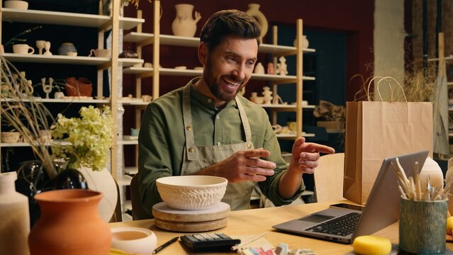 Craftsman Caucasian man male small business owner businessman potter blogger seller talking video call lesson waving hand explaining ceramic recording online blog sell pottery laptop indoors workshop - Powered by Adobe
