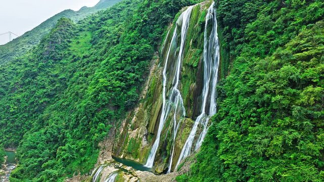 Aerial shot of beautiful waterfall cascading down the green mountain cliff in natural landscape
