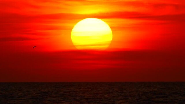 Sunset ocean red sky, intense yellow sun shines brightly over dark water.