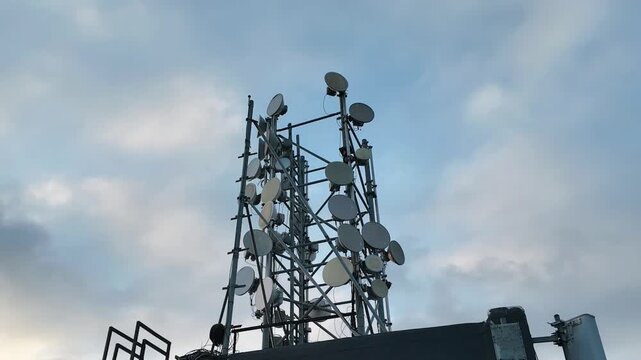 Rooftop base station with antennas and lightning rod under moving clouds. Telecommunication infrastructure time-lapse video showing wireless technology and modern urban skyline.