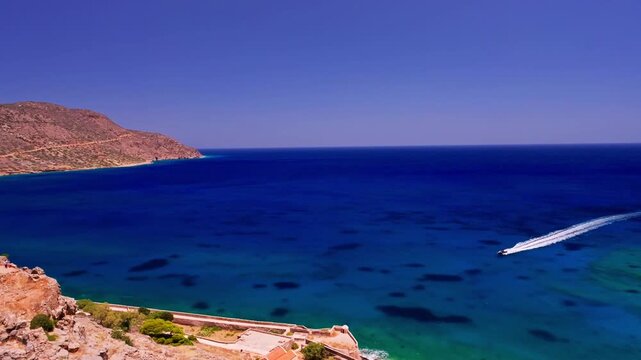 Aerial view of the historic Spinalonga fortress surrounded by the turquoise waters of the sea, a boat cutting through the waves, Elounda, lasithi, Greece.