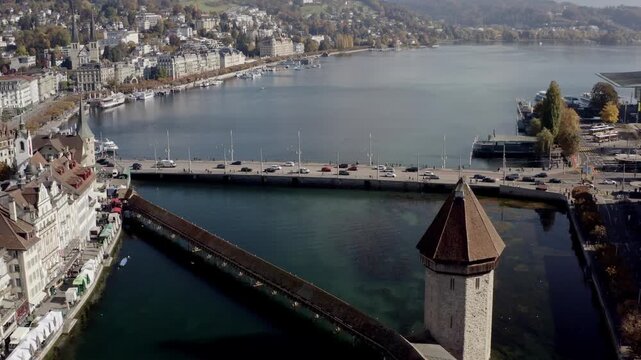 Aerial view of the Chapel Bridge and Wasserturm over the Reuss River, reflecting the clear sky, with buildings lining the shore, lucerne, lucerne, Switzerland.