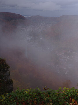 Clifftop overlook of Mist Shrouded Autumn Valley with Foggy Hills, Forests and a Quiet Town