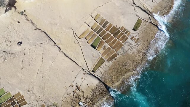 Aerial view of geometric salt pans next to the turquoise ocean, a beautiful contrast of man-made structures and natural beauty, Gozo island, Gozo, Malta.